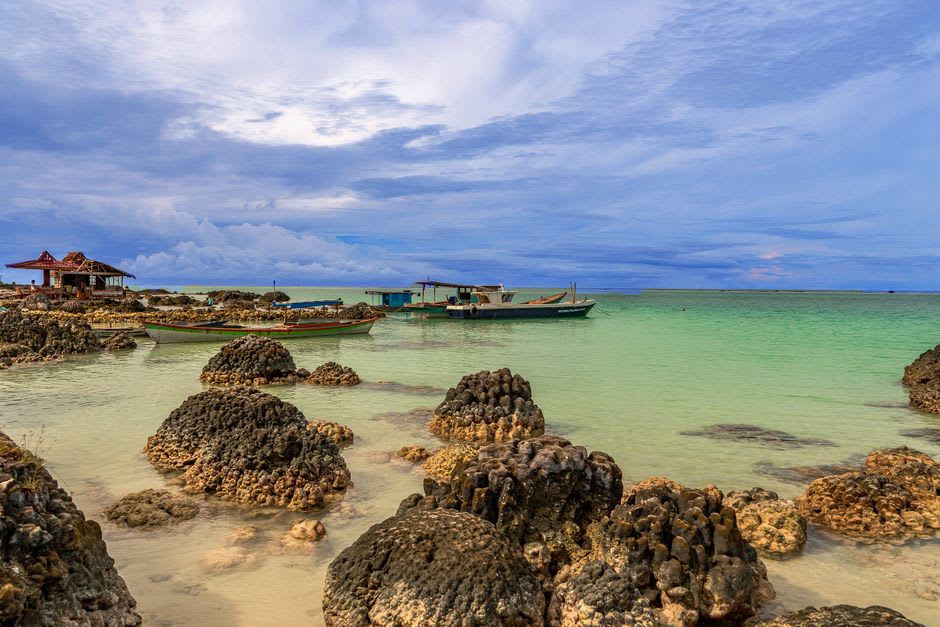 Fishing boats pulled up on the coral-sand beach at Calibishie with the village visible behind
