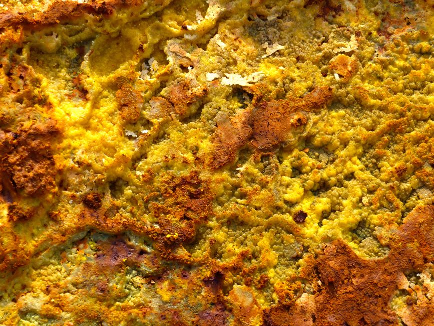A guide standing beside a bubbling grey mud pool at Soufriere Sulphur Springs, sulphur-stained rocks surrounding it