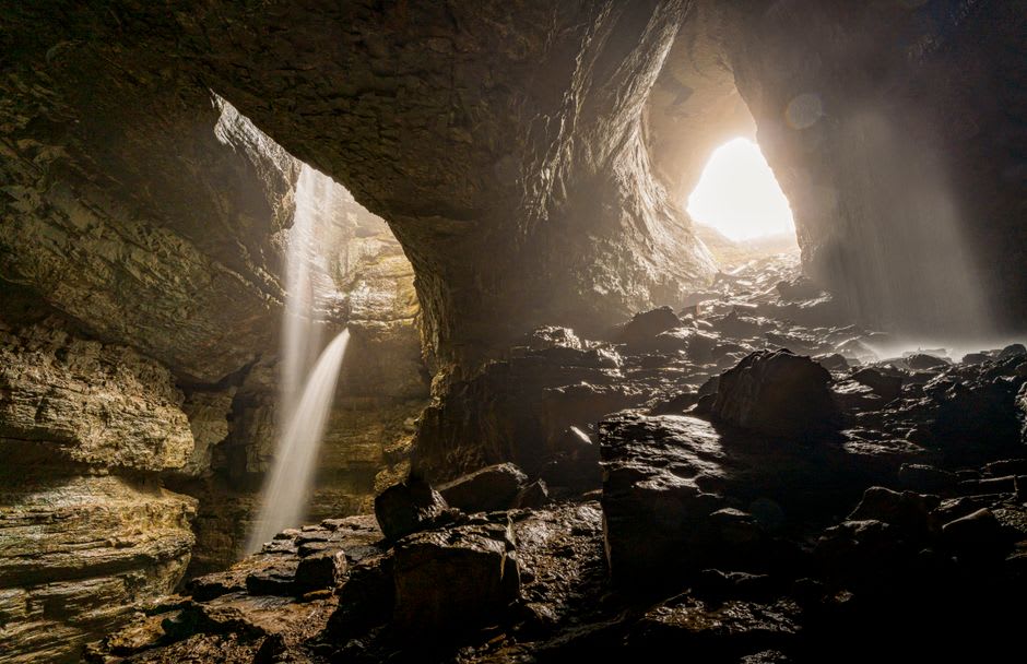 Small waterfall inside the enclosed chamber at the far end of Titou Gorge, swimmers floating in the pool below