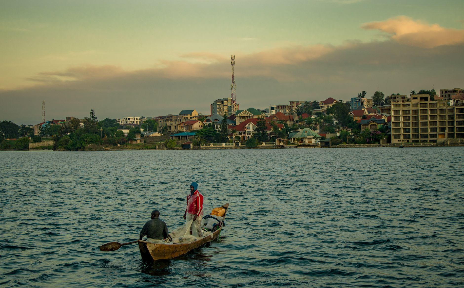 El lago Tanganica cerca de la orilla de Kalemie, el agua azul-verde cristalina captando la luz de la tarde, colinas abruptas del rift elevándose al fondo