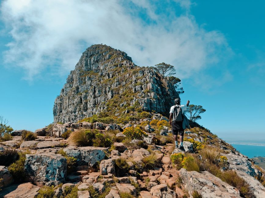 Hikers walking the trail toward a rock shelter entrance in Didima Gorge with the Drakensberg escarpment behind them