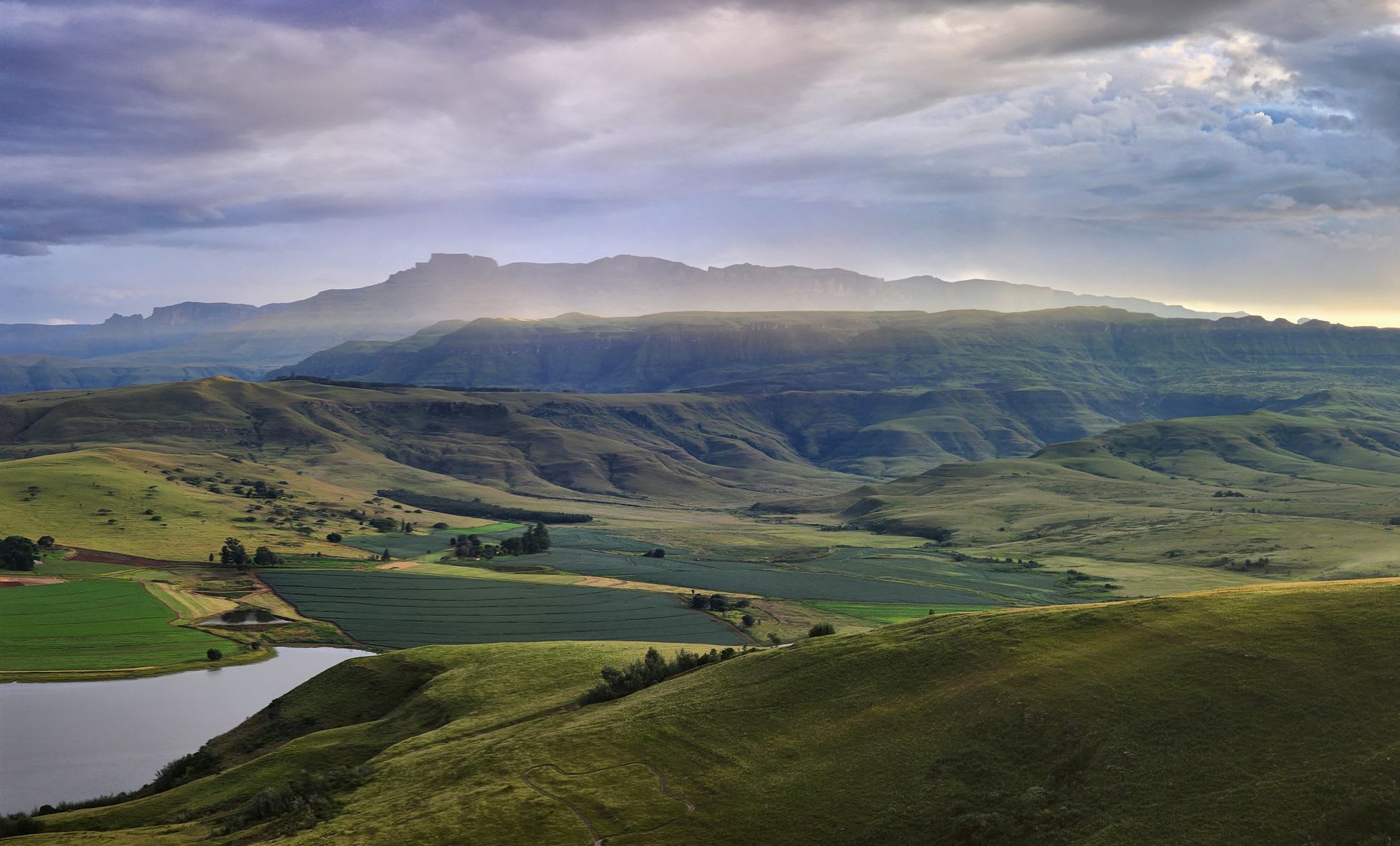 Hikers crossing a wooden bridge over the Tugela River in the valley below the Amphitheatre at golden hour