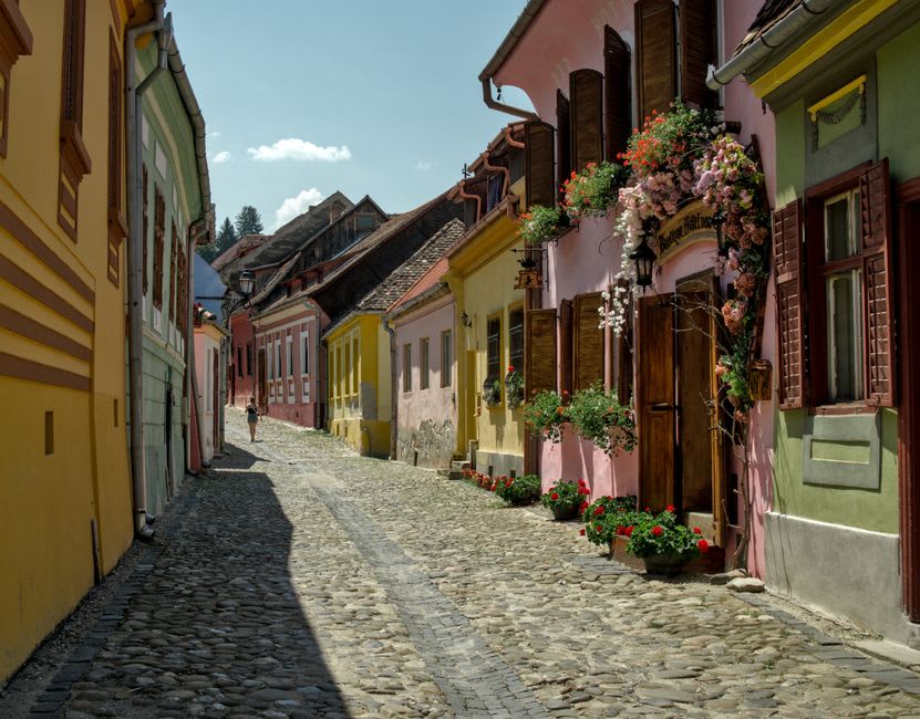 Una calle empedrada y estrecha en Alegría bordeada de casas pintadas en colores brillantes y balcones desbordantes de flores