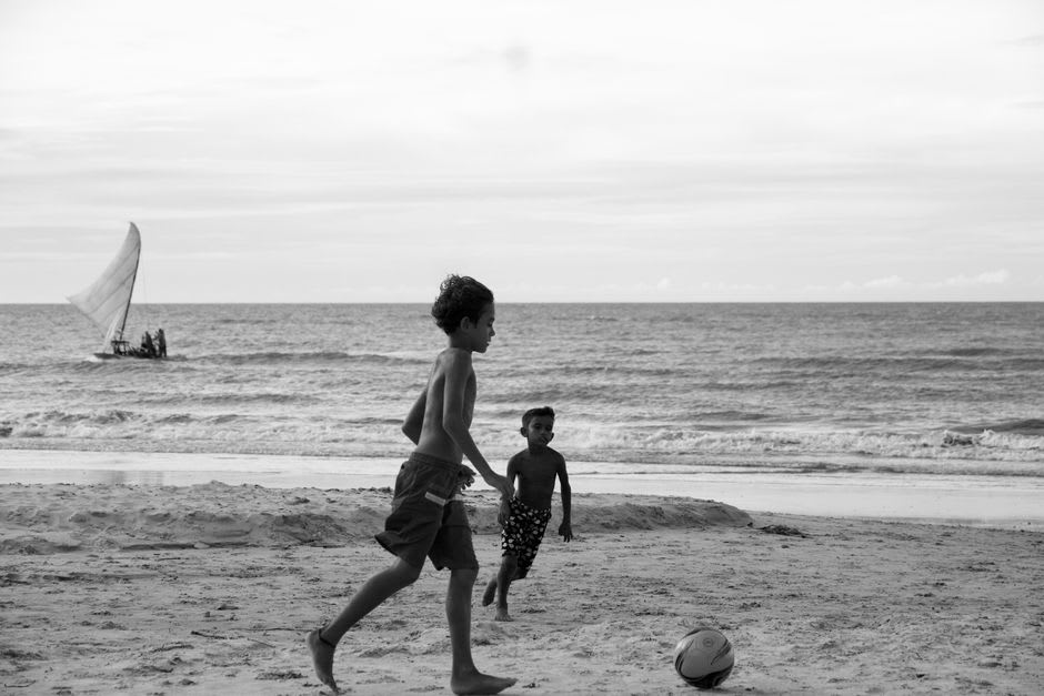 Kids playing barefoot soccer on the wide sand beach at El Cuco as fishermen prepare boats in the background