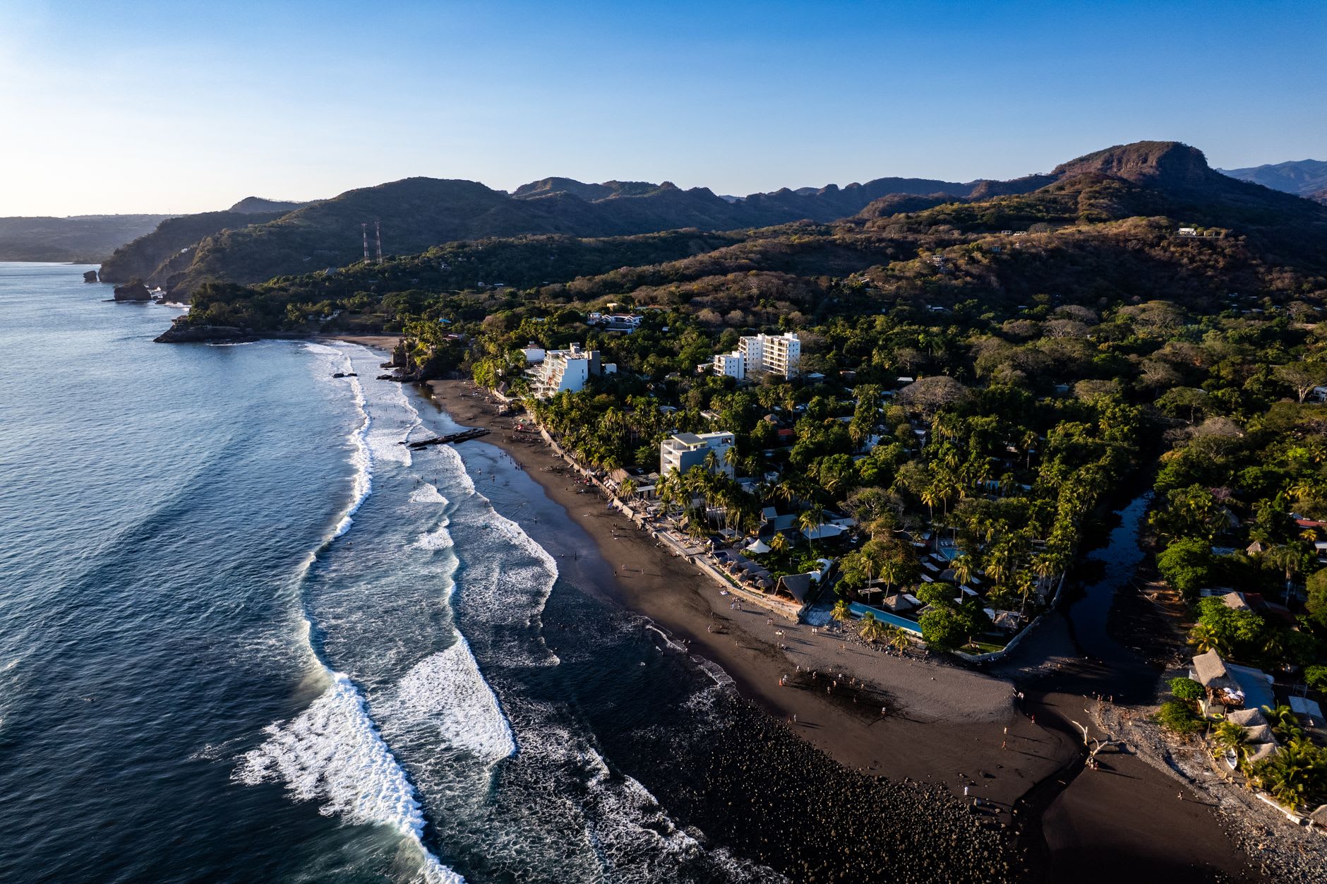 The black volcanic sand beach at El Tunco at sunset with the Pacific crashing onto the rocks