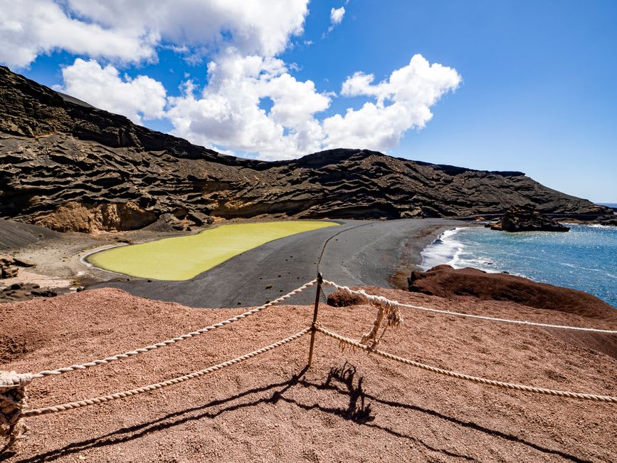 The steep trail descending into the crater toward the shoreline of Laguna de Alegría, mineral deposits staining the rocks
