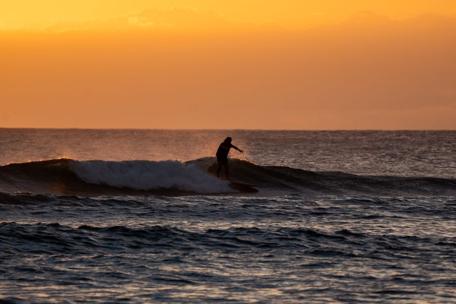 A surfer riding a wave at the point break at Playa El Zonte as the sun sets over the Pacific