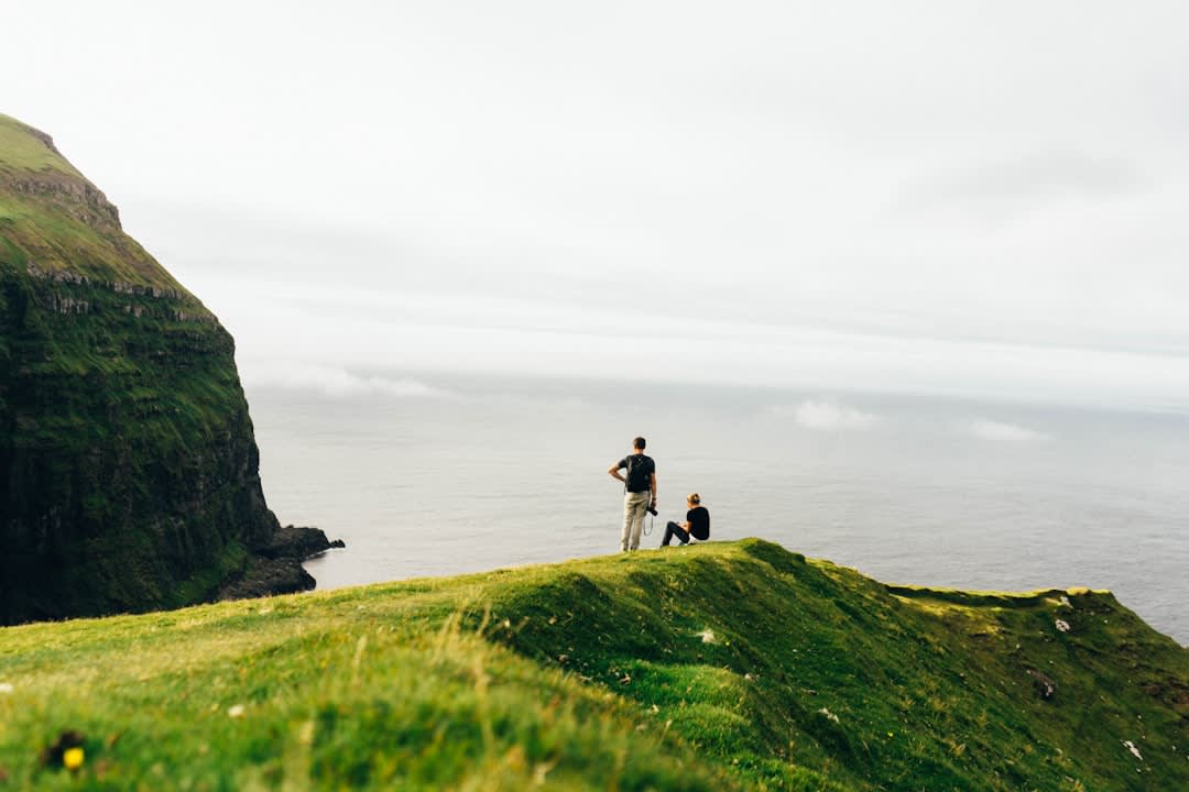 Hikers walking the grassy ridge trail toward Kallur Lighthouse on Kalsoy