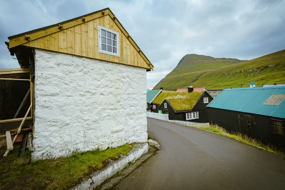 A memorial bench in the village of Trøllanes on Kalsoy with turf-roofed houses in the background