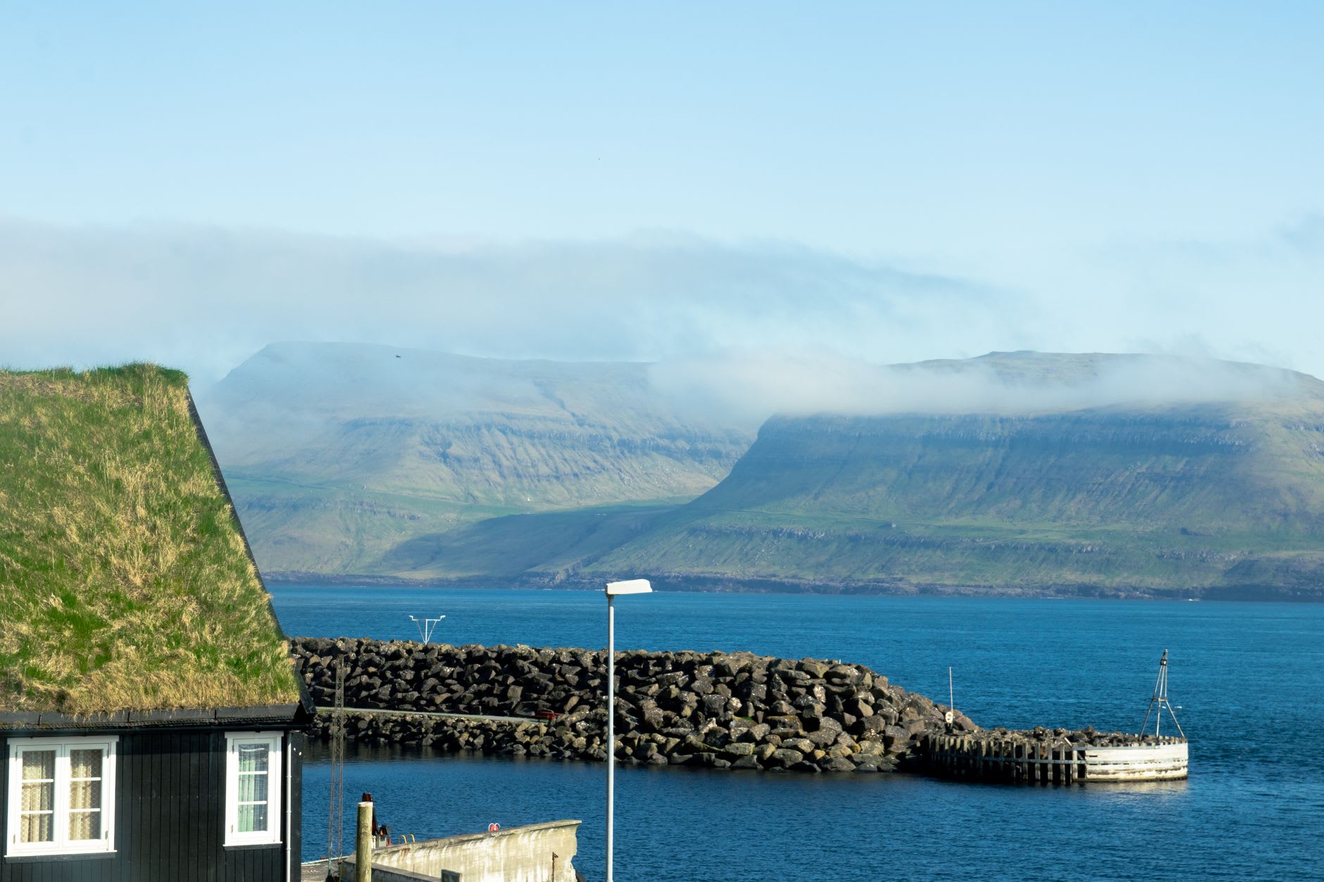 Las paredes de arenisca roja sin techo de la Catedral de Magnus en Kirkjubøur enmarcando un cielo pálido, con vista al mar a través de las ventanas en arco