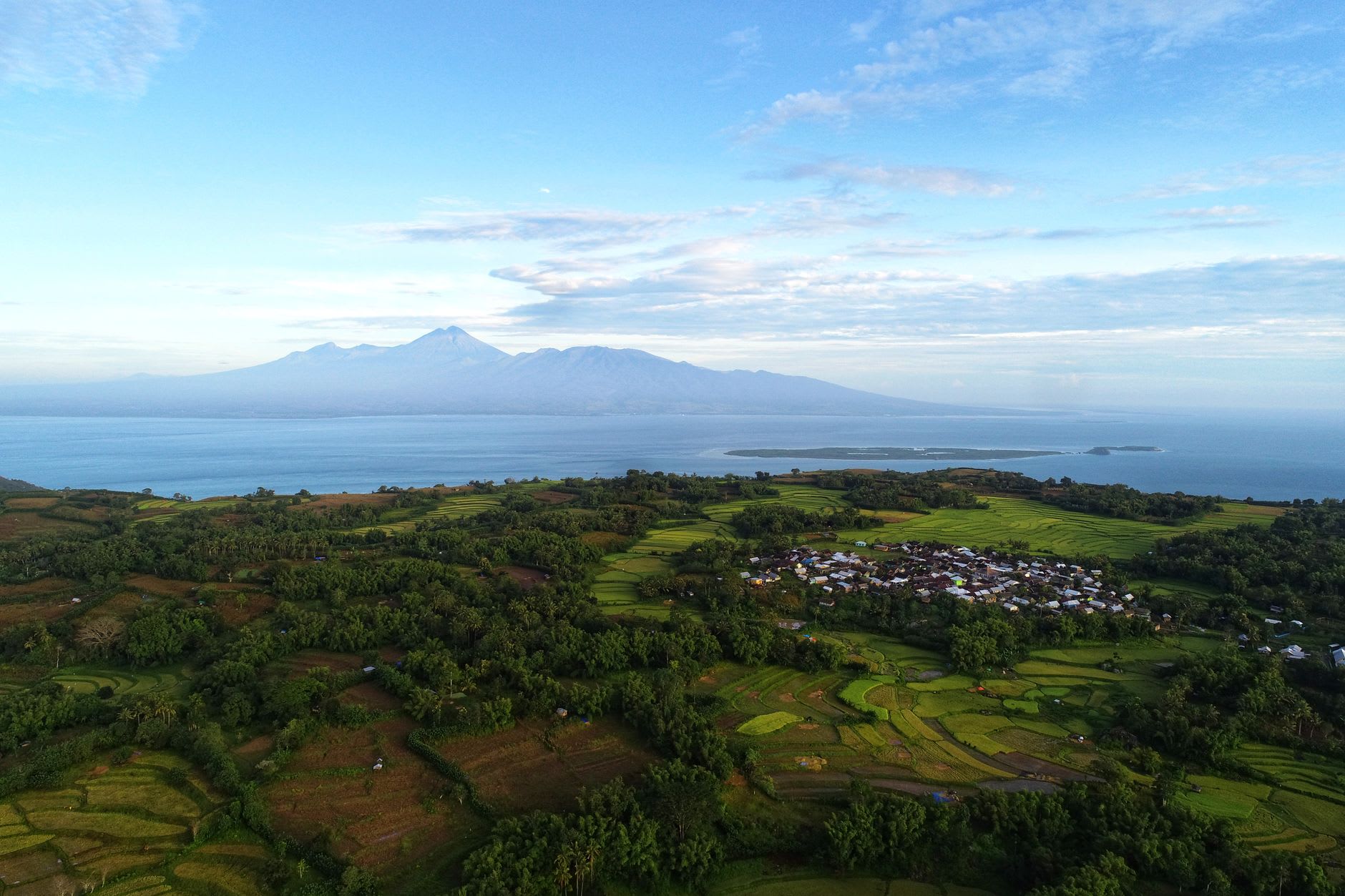 The Cathedral of San Yosep in Larantuka, a white colonial church with red roof at golden hour, mountains and sea visible behind