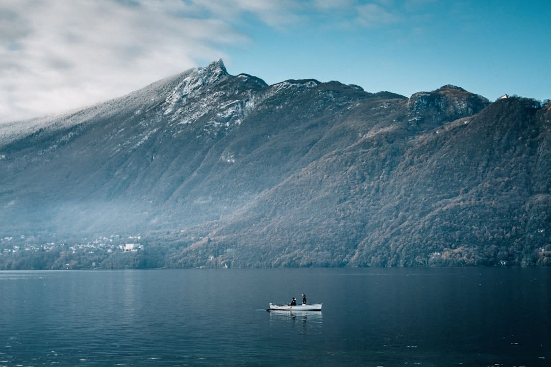 The still grey-blue water of Lac du Bourget at dawn with wooded mountains reflected on the surface