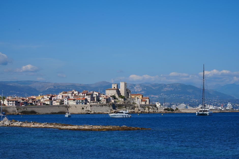 The old stone sea ramparts of Antibes with fishing boats moored below and the Alps visible across the bay