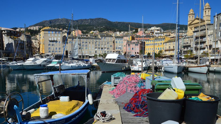 Bastia's Vieux Port at dawn, fishing boats moored below ochre and salmon-colored buildings with faded shutters
