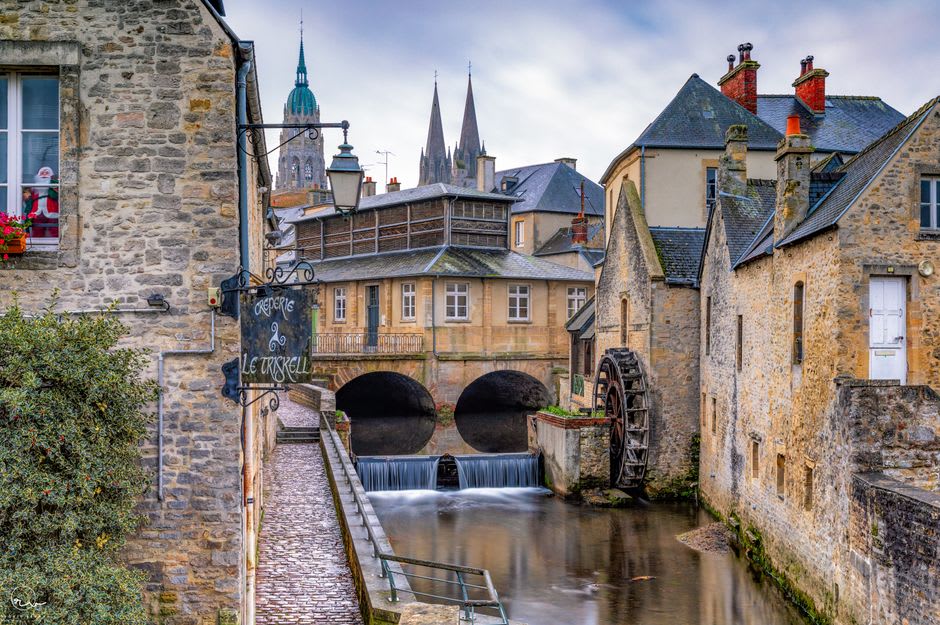 Stone footbridges and old watermills along the narrow channels of the Aure river through Bayeux's historic centre