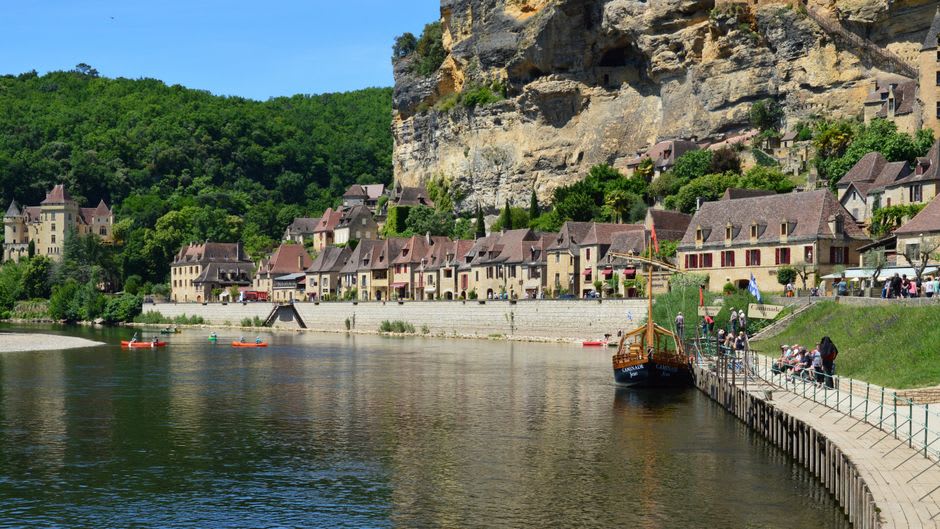 A traditional gabarre river boat drifting on the Dordogne River beneath the cliffside village of Beynac