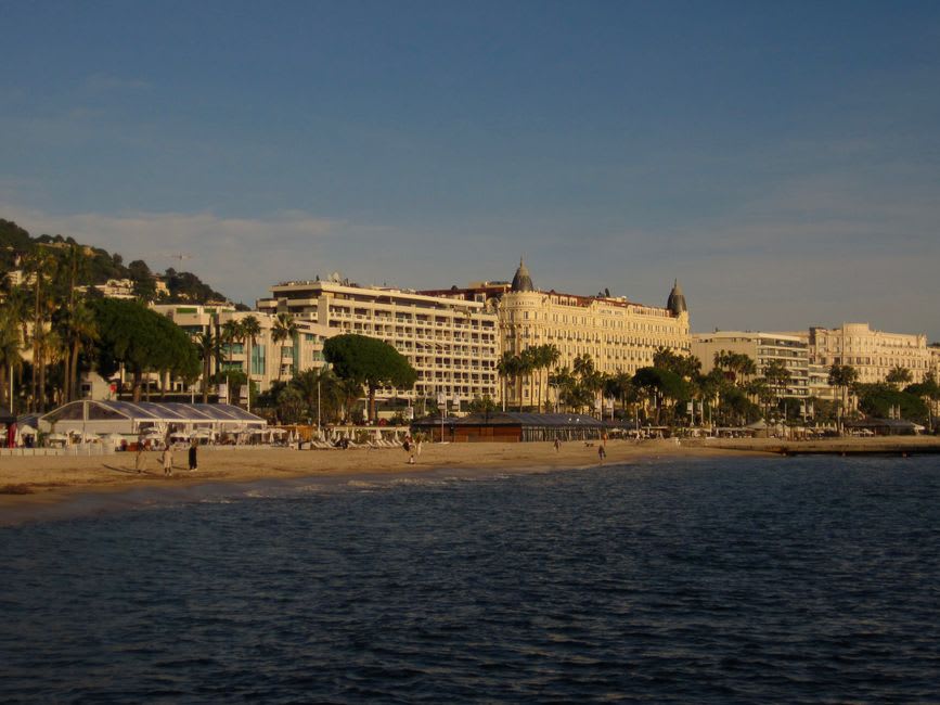 The palm-lined boulevard of La Croisette in Cannes with grand hotels and the bay in the background at sunset