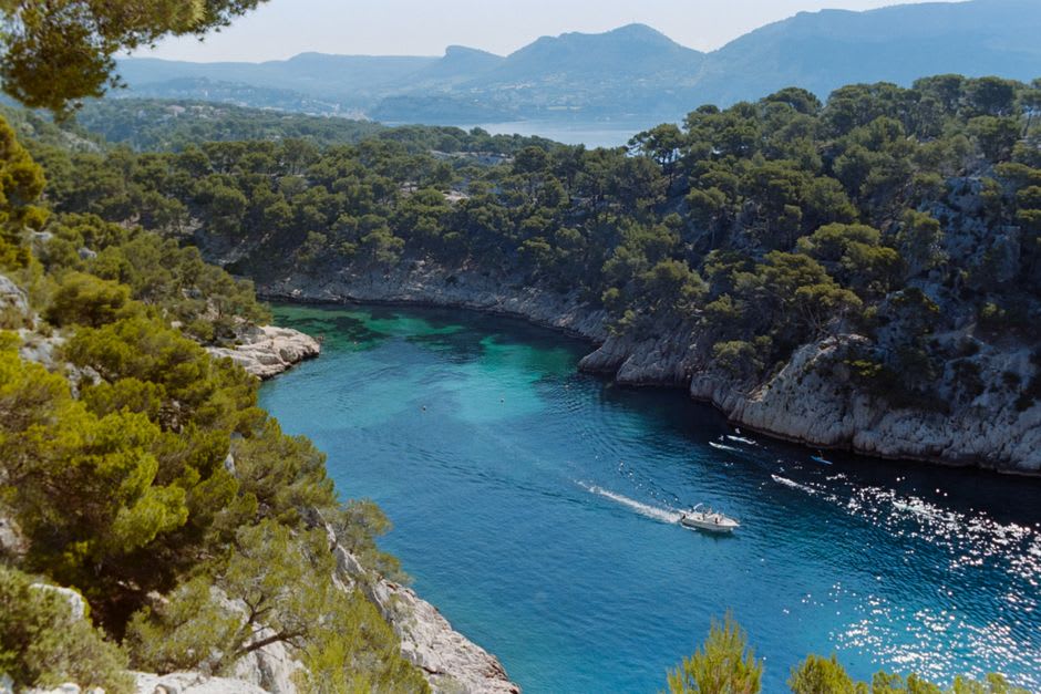 A boat gliding through a narrow turquoise calanque between towering white limestone cliffs near Cassis