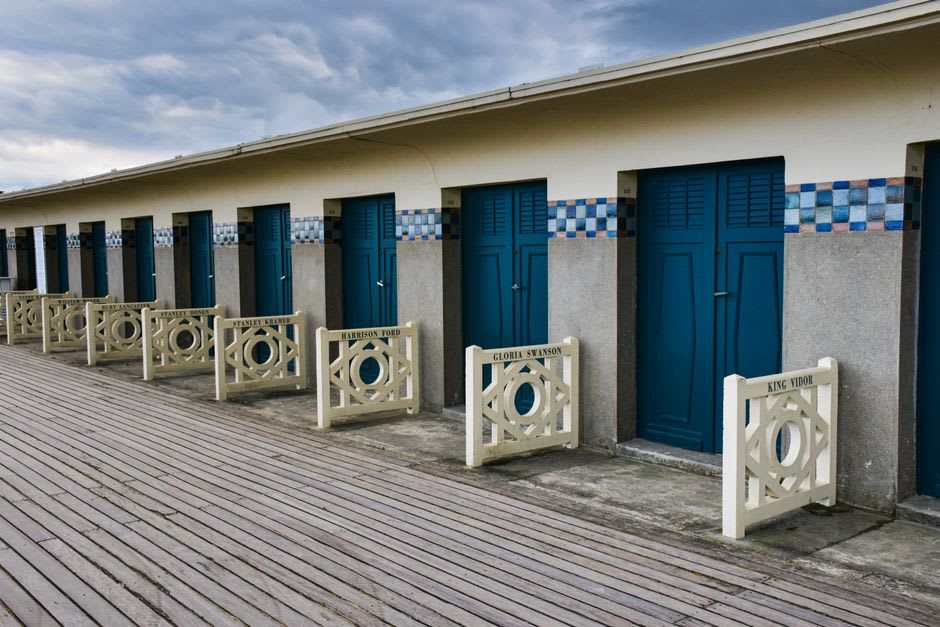 The wooden boardwalk of Les Planches in Deauville lined with named beach cabins and striped umbrellas
