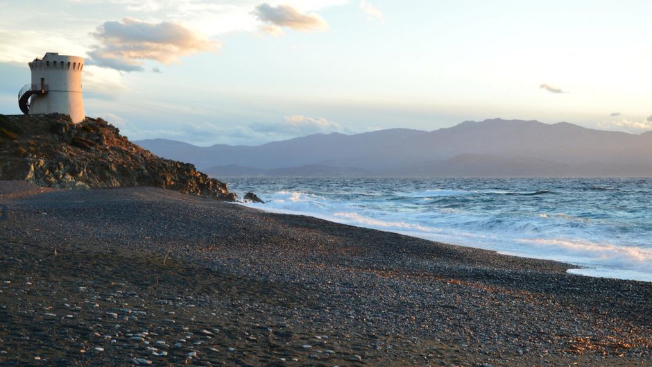 The crumbling Genoese watchtower on Erbalunga's rocky point at dusk, waves breaking against its base
