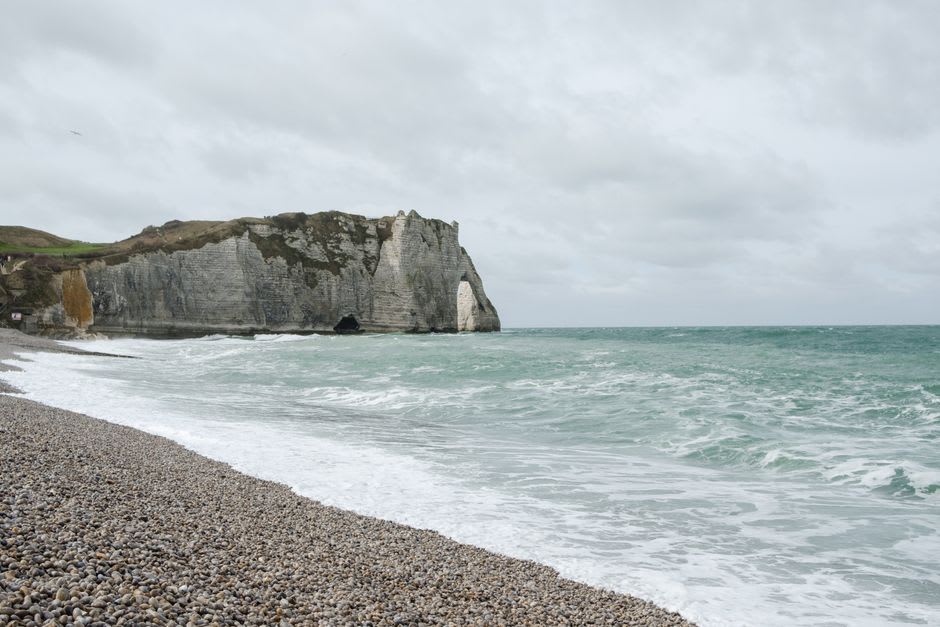 The pebble beach at Étretat with the white chalk Falaise d'Amont and its clifftop chapel in the distance