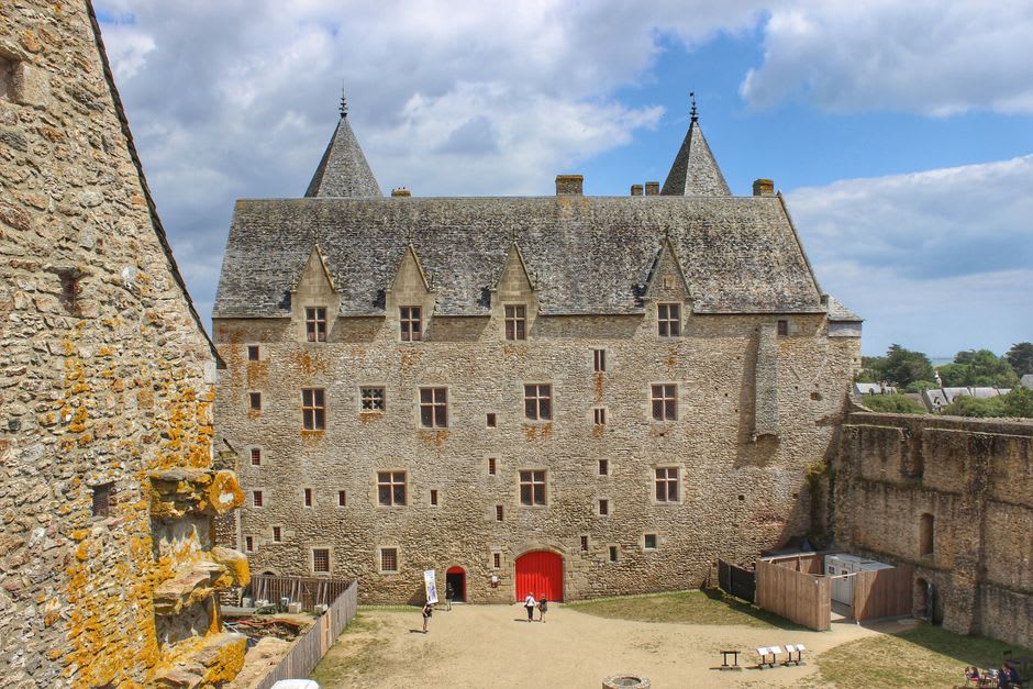 The weathered stone walls of Excideuil's twin medieval towers seen from the castle courtyard, with wooded hills visible beyond