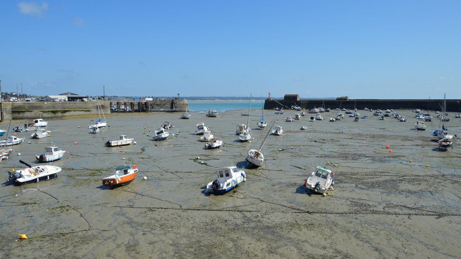 Fishing boats moored at low tide in Granville's harbour with the fortified Haute Ville rising above on the headland