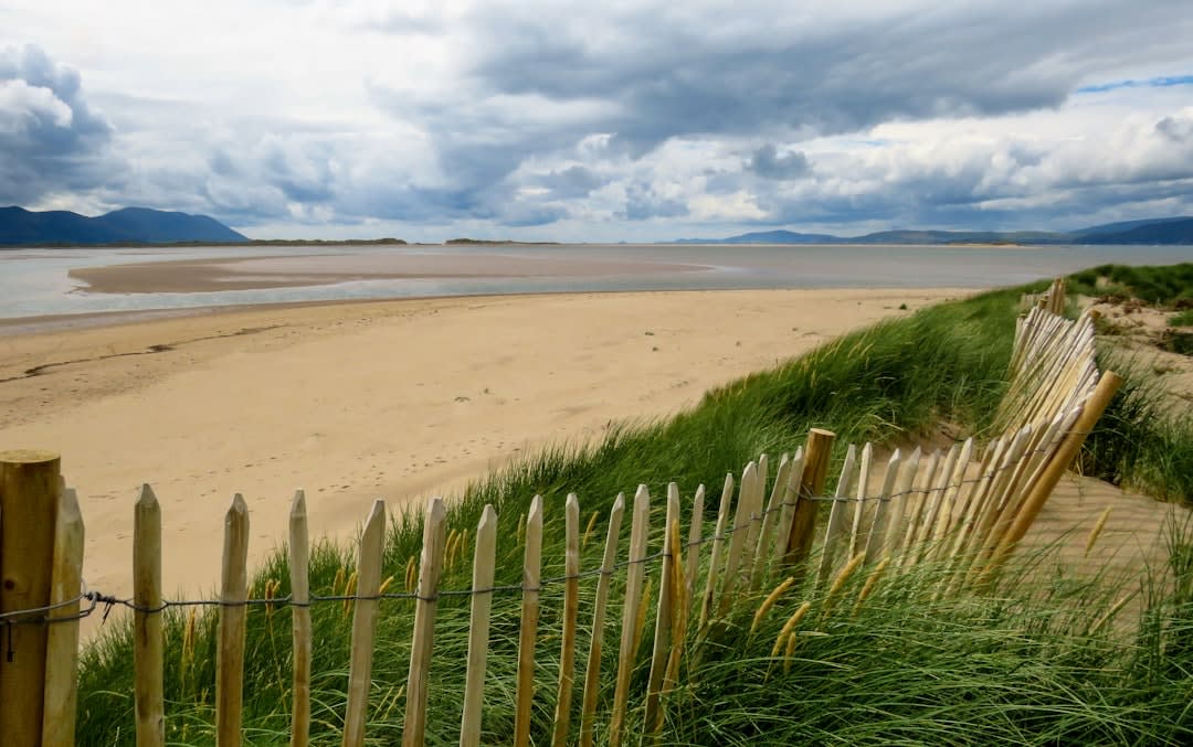 A wide sandy beach stretching east from L'Île-Rousse's harbor, the coastal railway track visible along the shore