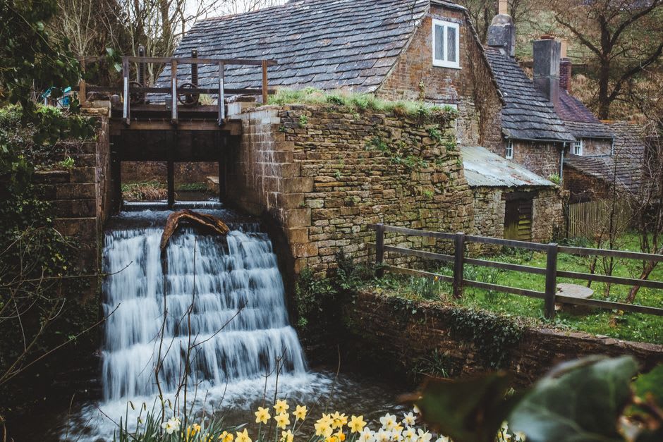 A moss-covered wooden waterwheel turning beside a stone bridge over the clear Sorgue river