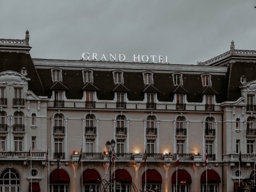 A grand Belle Époque hotel facade with pastel stone and wrought-iron balconies along a promenade in La Bourboule
