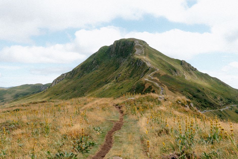 Hikers on the rocky summit trail of the Puy de Sancy with the green volcanic Chaîne des Puys stretching into the distance