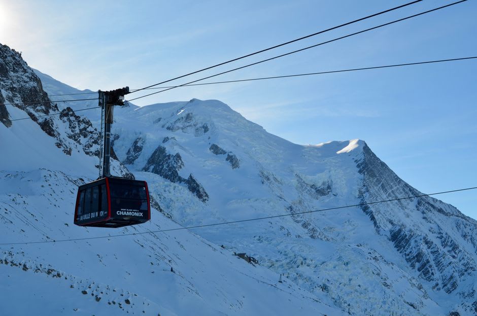 The narrow-gauge Tramway du Mont-Blanc train climbing a mountainside track above Les Houches toward glaciers