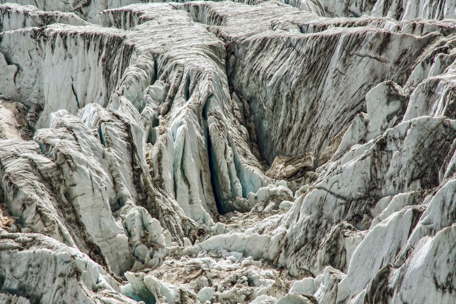 The crevassed white ice of the Bossons glacier descending toward pine forest above Les Houches