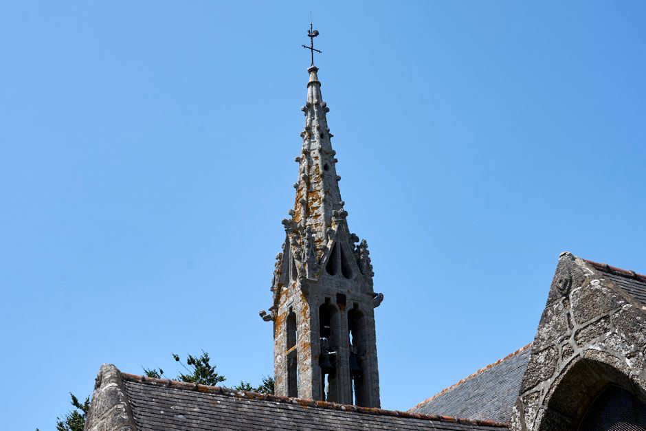 The Église Saint-Ronan and its granite spire seen from a wooded hillside above Locronan with the sea in the distance
