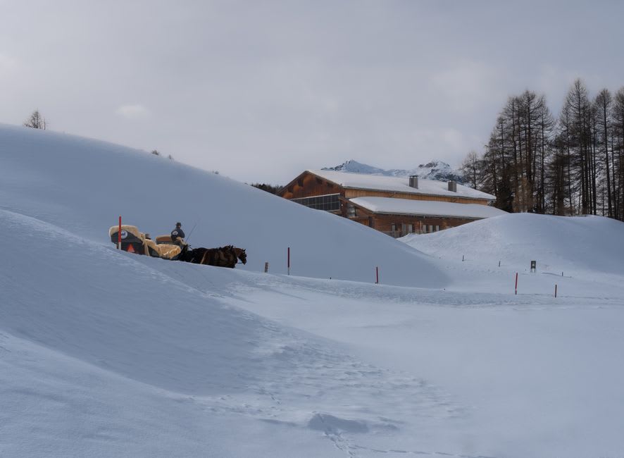 Horse-drawn sleigh crossing a snowy square in front of Megève's old stone church