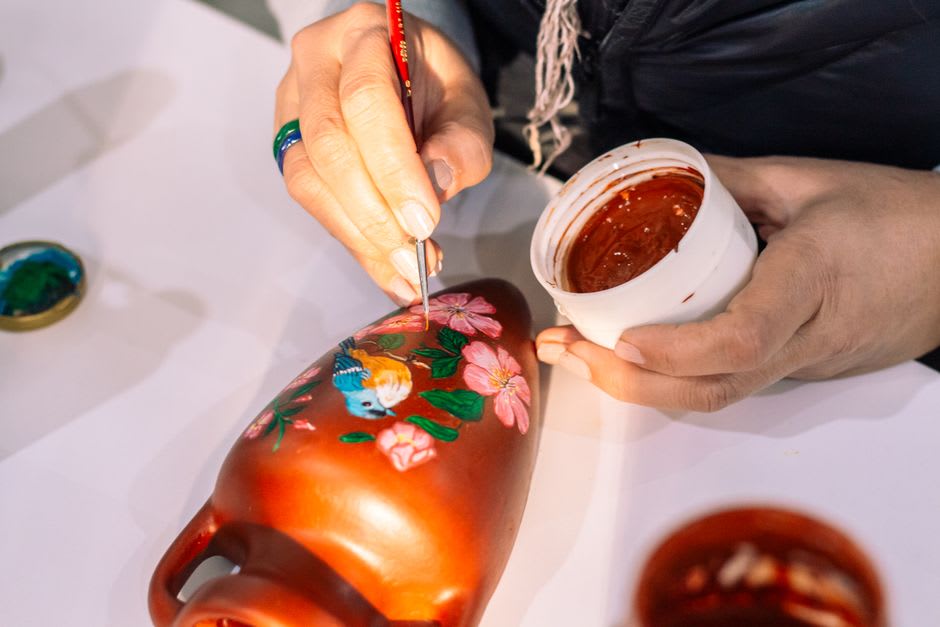 A potter's hands painting a delicate blue hunting scene onto white faience pottery in a Moustiers-Sainte-Marie workshop