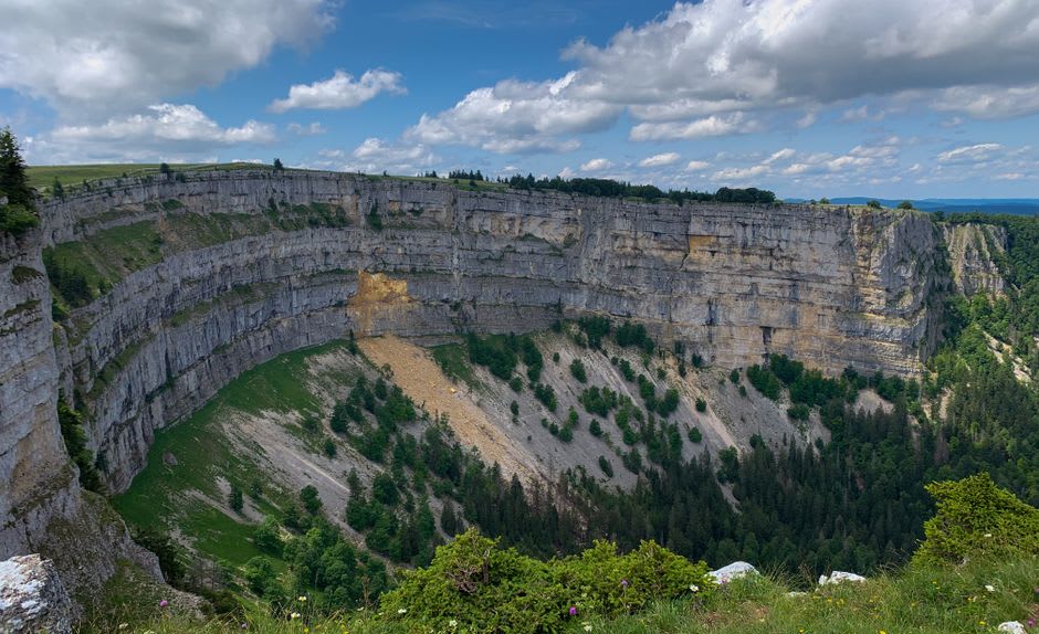 The Source du Doubs emerging as a clear spring at the base of a limestone rock face in the forest near Mouthe