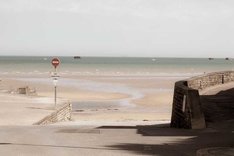 Rusting remnants of the Mulberry harbour structures visible in the shallow water off Omaha Beach