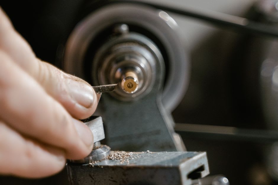 A craftsman's hands carving a briar pipe bowl on a lathe in a small Saint-Claude workshop