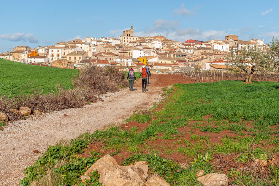 Pilgrims with backpacks and scallop shells walking down the steep stone rue de la Citadelle in Saint-Jean-Pied-de-Port