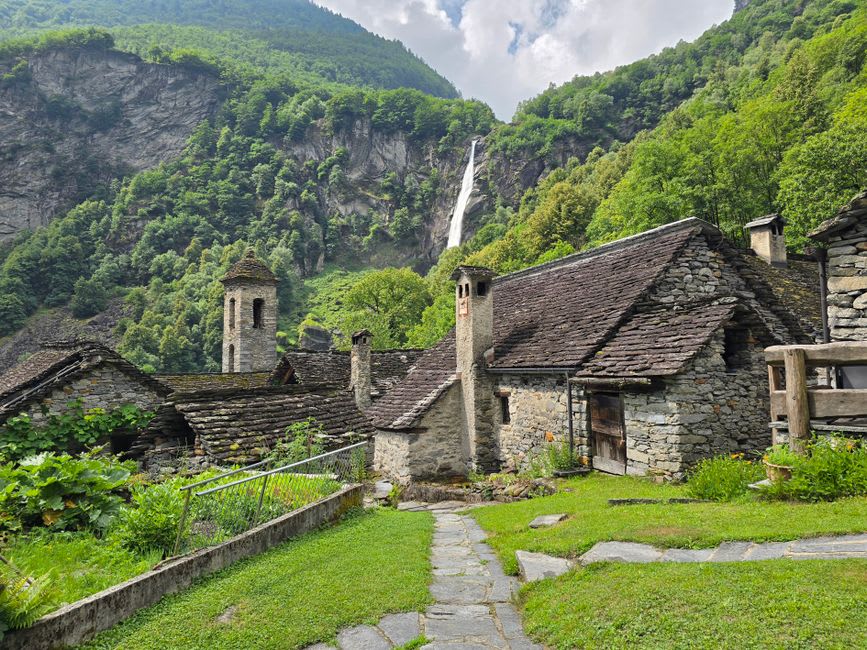 A stone path winding through terraced alpine plant beds and a small waterfall in the Jardin Botanique Alpin de la Jaÿsinia