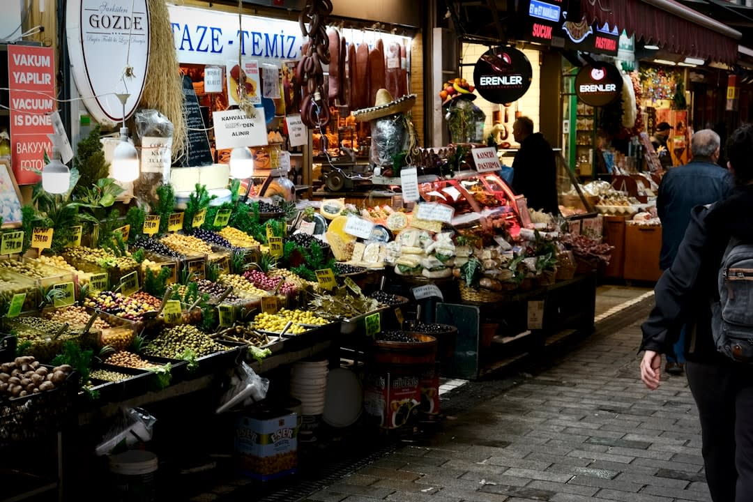 A crowded Saturday market stall in Sarlat piled with duck confit, foie gras, and walnuts under the old town's stone arcades
