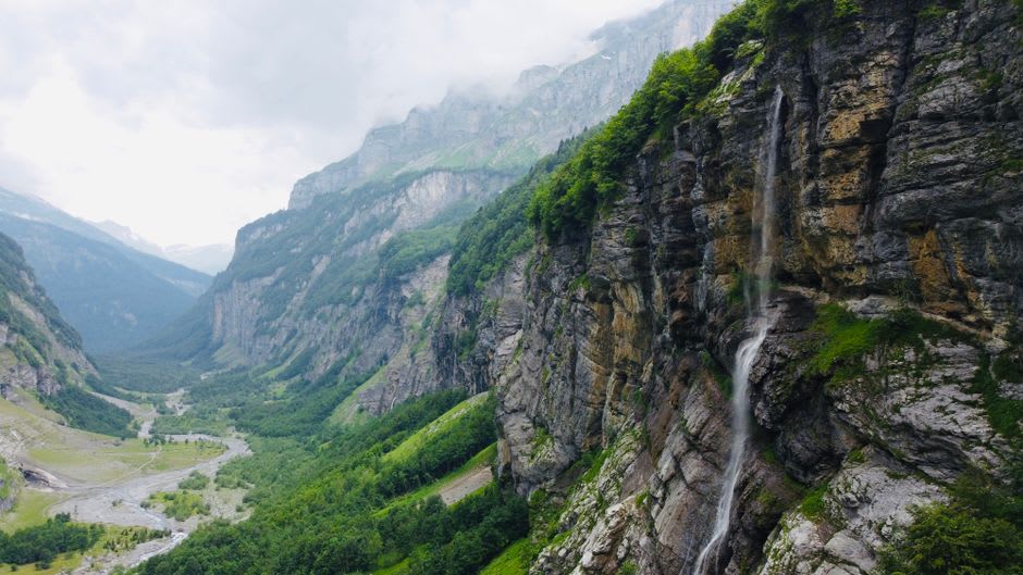 The horseshoe cliffs of the Cirque du Fer-à-Cheval with multiple waterfalls falling from the rim into a green glacial valley