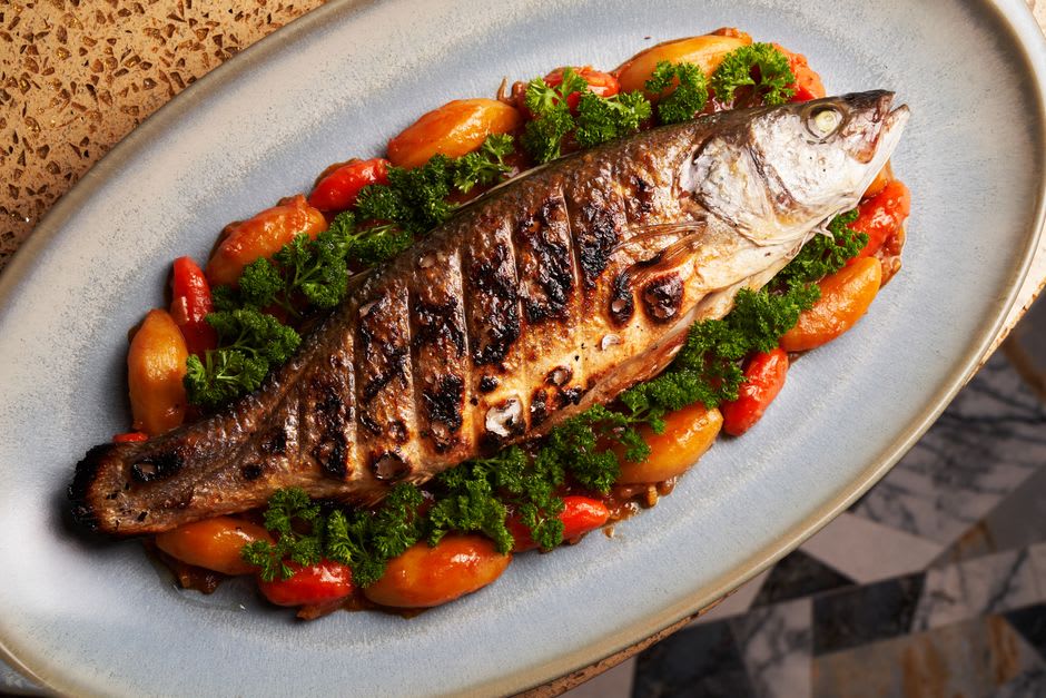 A grilled whole féra fish served on a plate at a lakeside restaurant table in Talloires with Lac d'Annecy in the background