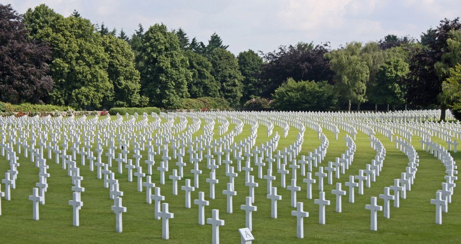 Rows of white crosses stretching toward the pale stone tower of the Ossuaire de Douaumont under a grey sky