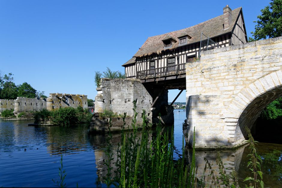The stone piers of Vernon's ruined Vieux-Moulin bridge in the Seine, with a weathered half-timbered mill house perched above the water