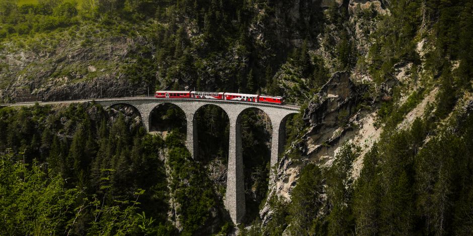 The yellow carriages of the Petit Train Jaune crossing a stone viaduct high above the Cerdagne valley