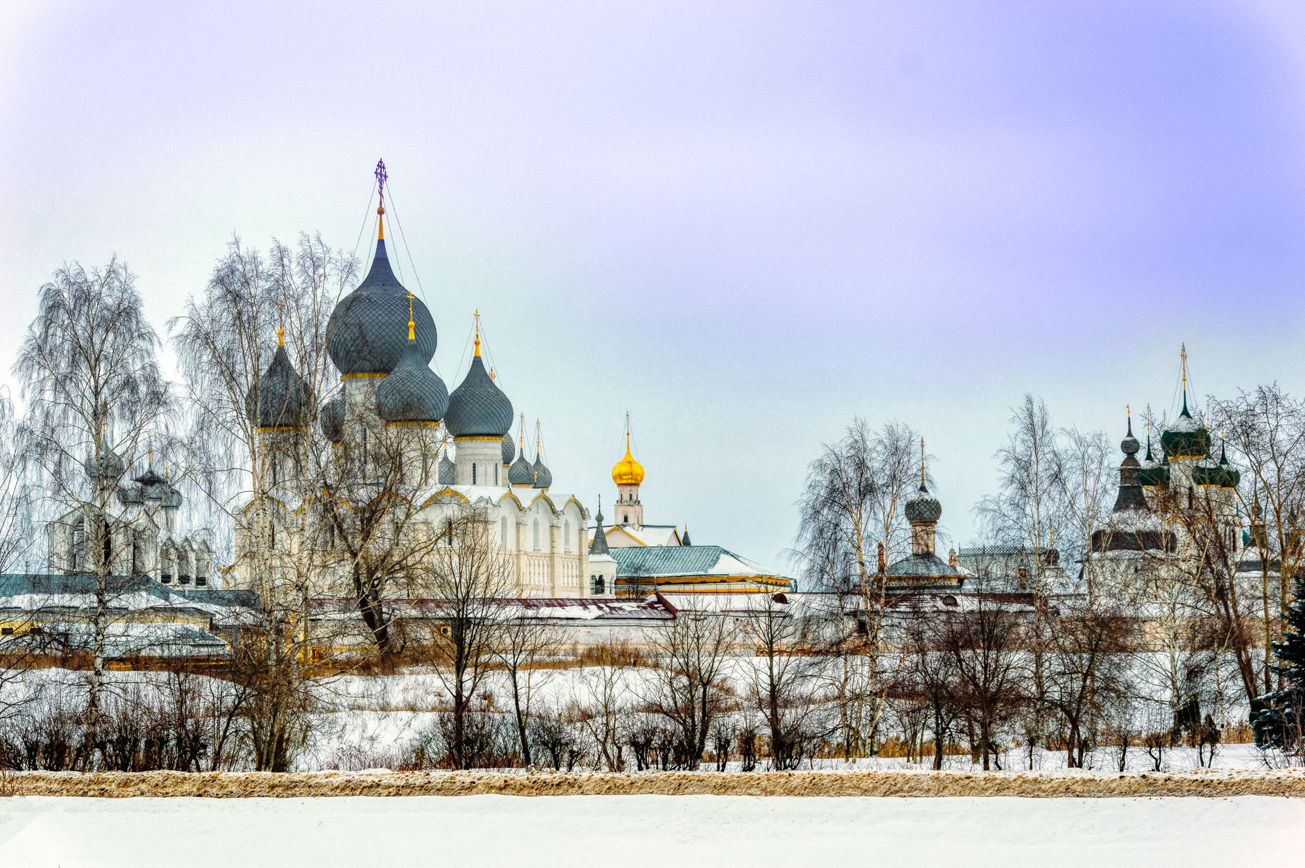 A lone ice fisherman on frozen Lake Nero in winter, Rostov Kremlin visible as a silhouette in the far background