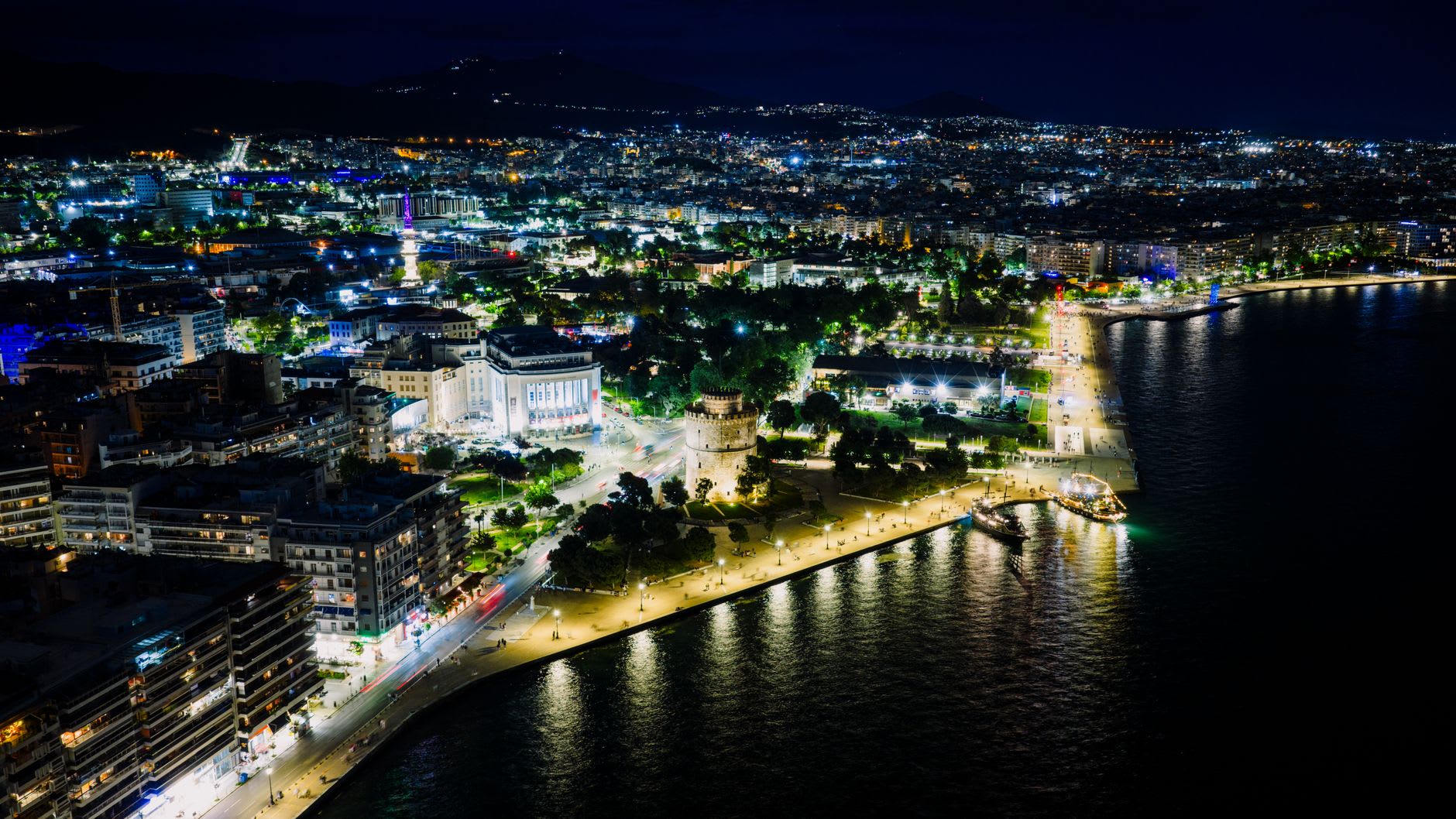 The White Tower of Thessaloniki glowing amber at night reflected in the Thermaic Gulf waterfront promenade