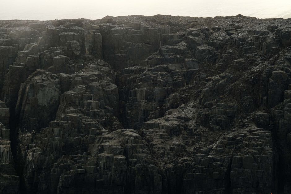 Acantilados de basalto elevándose sobre la costa de arena negra cerca de Qeqertarsuaq